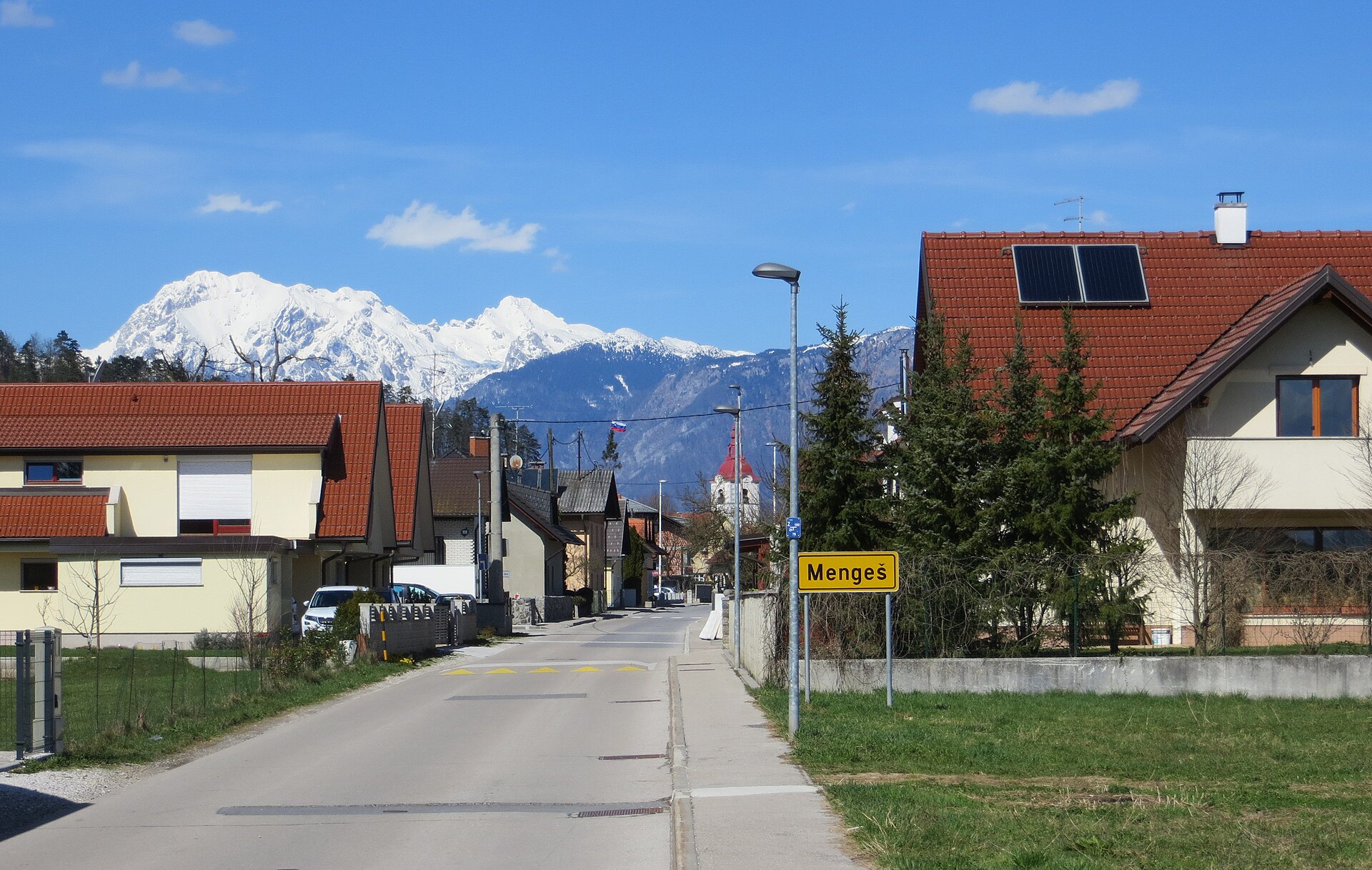 Ulica v Mengešu s hišami in snegom pokritimi gorami v ozadju